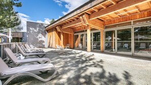A modern building with a wooden facade and large glass windows. There are outdoor lounge chairs and a concrete patio area.