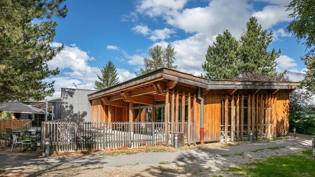A wooden building with a covered patio area, surrounded by trees.