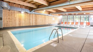 An indoor swimming pool with wooden panel walls, a concrete floor, and a row of orange chairs along the side.