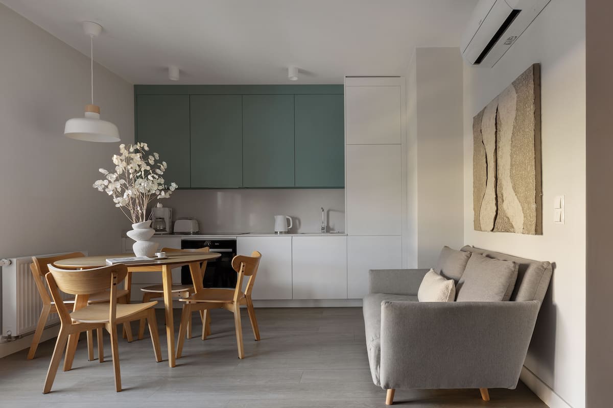 A modern kitchen with teal cabinets, a dining area with wooden chairs, and a grey sofa.