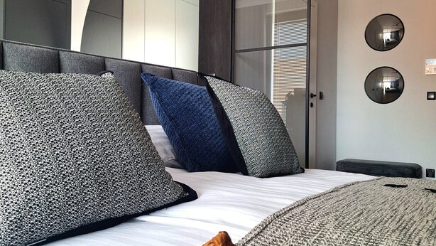 Une chambre à coucher moderne avec un lit, des oreillers, un plateau avec un croissant et un grand miroir au mur.