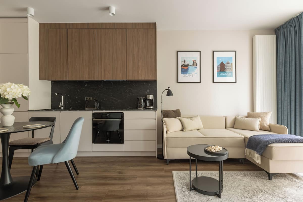 A modern living room with a sofa, a dining table, and a kitchen area with wooden cabinets and a black countertop.