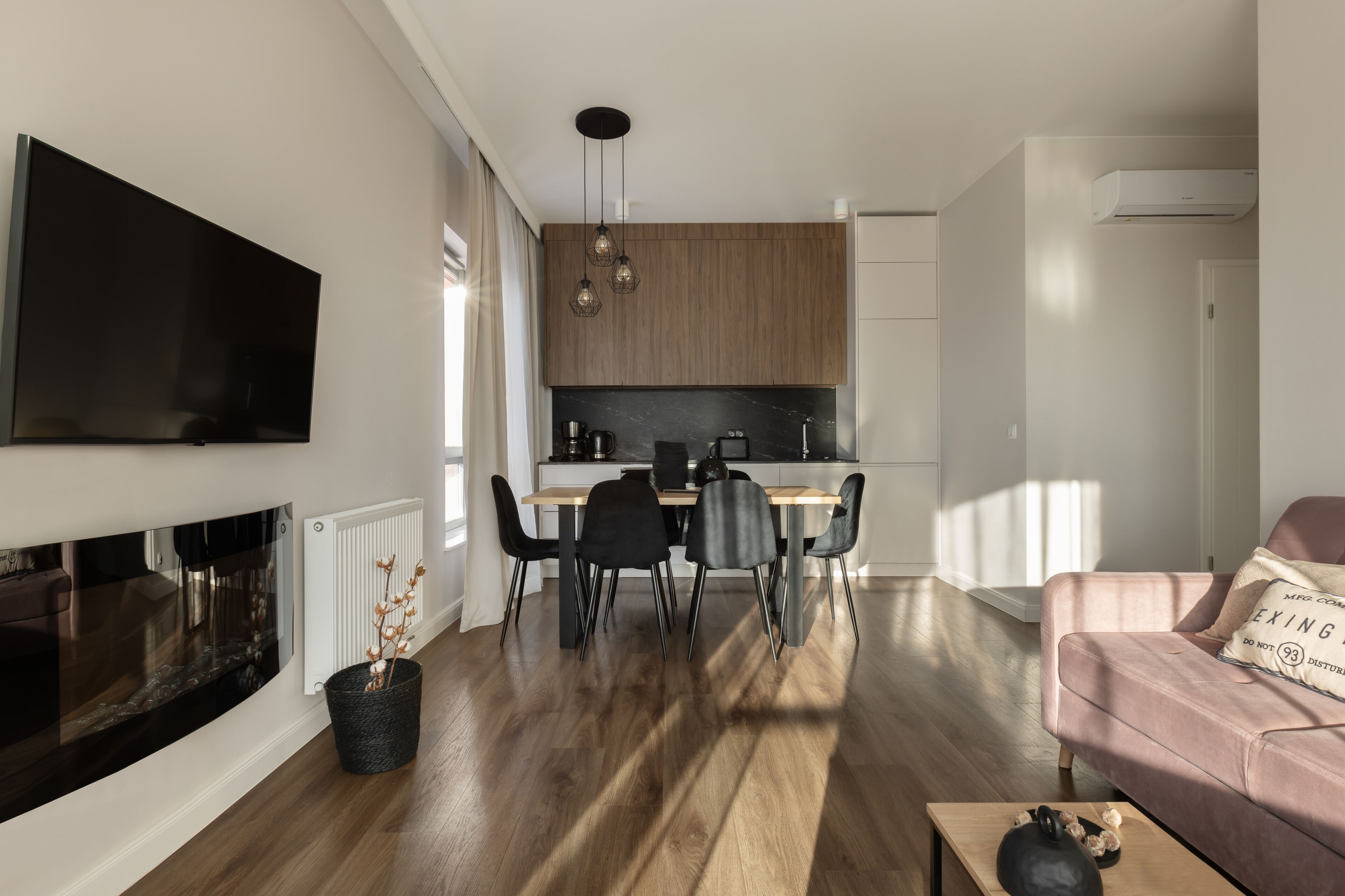 Un salon moderne avec une cheminée, un coin repas avec une cuisine en arrière-plan, et un canapé rose agrémenté d’un coussin.