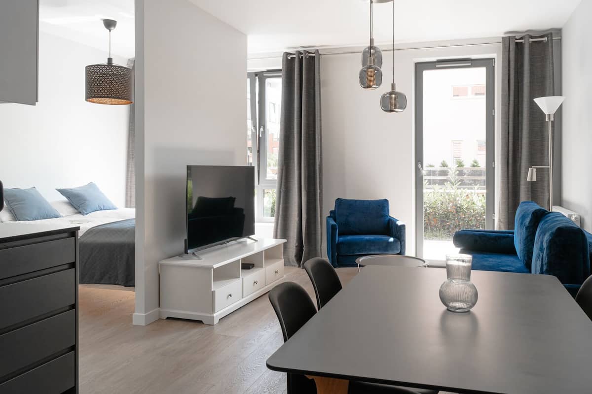 A modern living room with a flat-screen TV, a dining table, and two blue sofas.