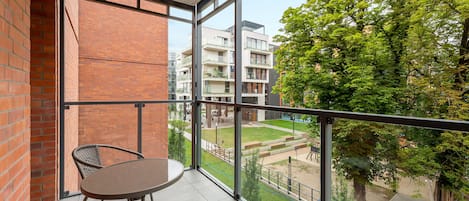 A balcony with a table and chairs, a view of a courtyard with buildings and trees.