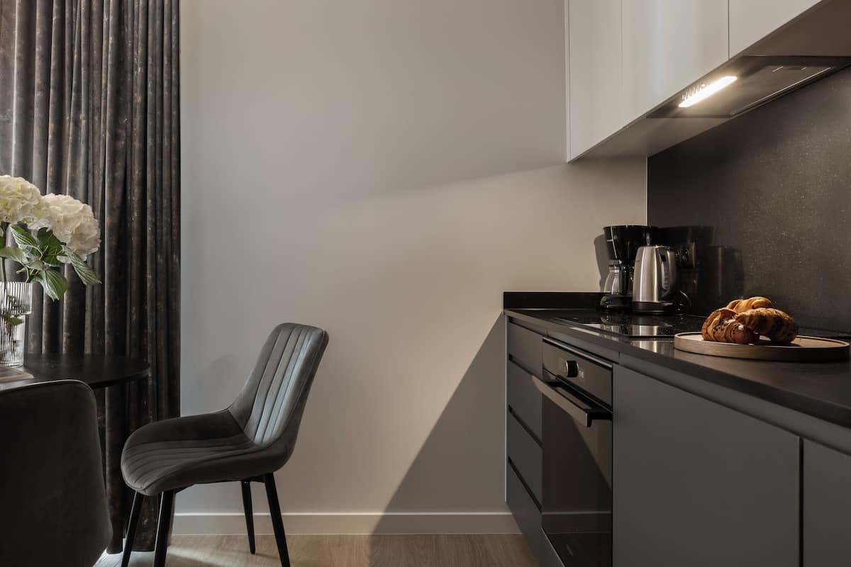 A modern kitchen with dark cabinetry, a black countertop, a coffee maker, and a plate with bread.