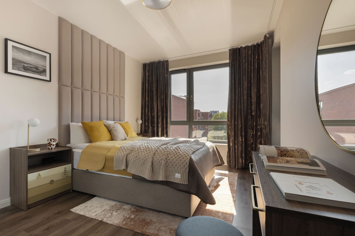 A modern bedroom with a bed, bedside table, and a large window with curtains.