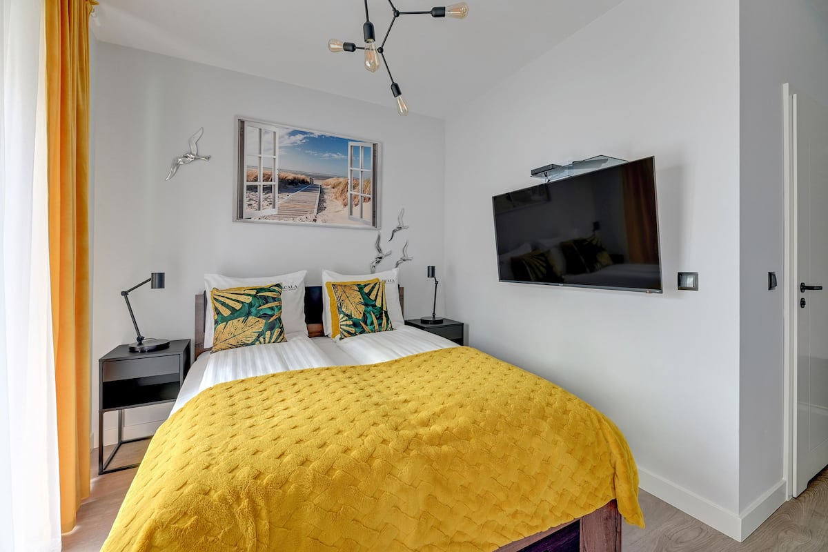 A modern bedroom with a large bed, a mounted TV, and a window with a beach view.