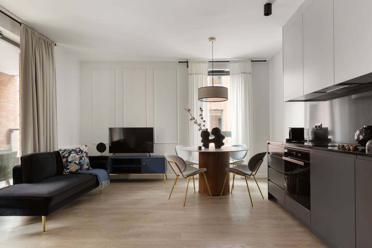 A modern living room with a sofa, TV, dining table, chairs, and a kitchen area.