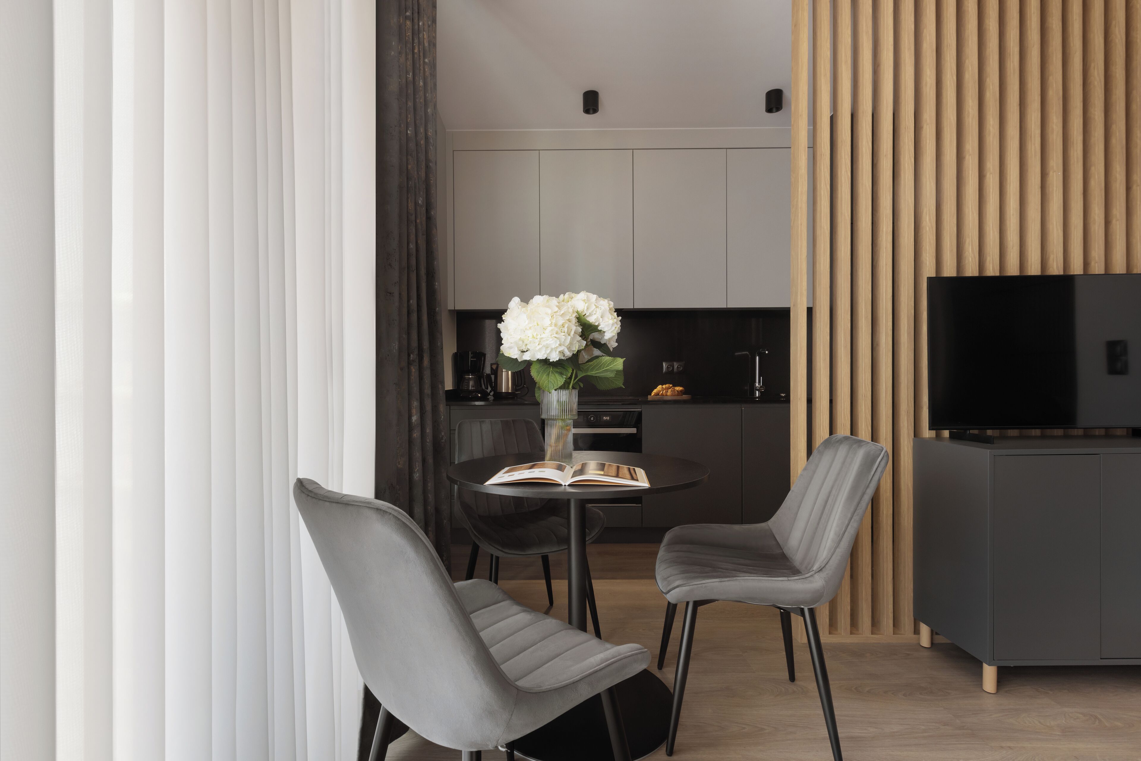 Een moderne eetruimte met een ronde tafel, twee grijze bekleden stoelen, een boek en een vaas met witte bloemen.