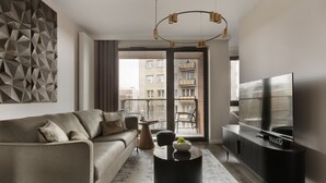 Un salon moderne avec un canapé, une table basse, un téléviseur et une grande fenêtre équipée de stores.