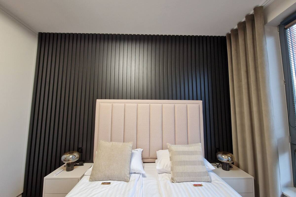 A double bed with a headboard, two bedside tables, and a window with curtains.