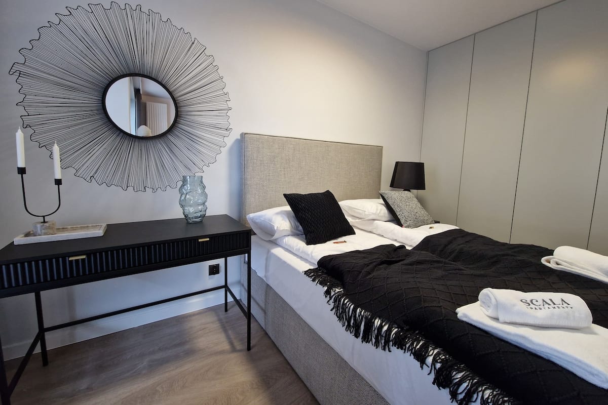 A modern bedroom with a bed, bedside table, and a large mirror.