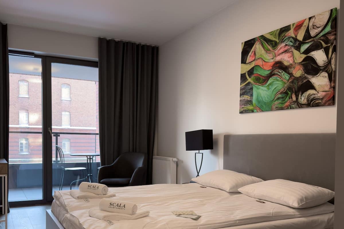 A modern hotel room with a large bed, a chair, a desk, and a view of the outside.