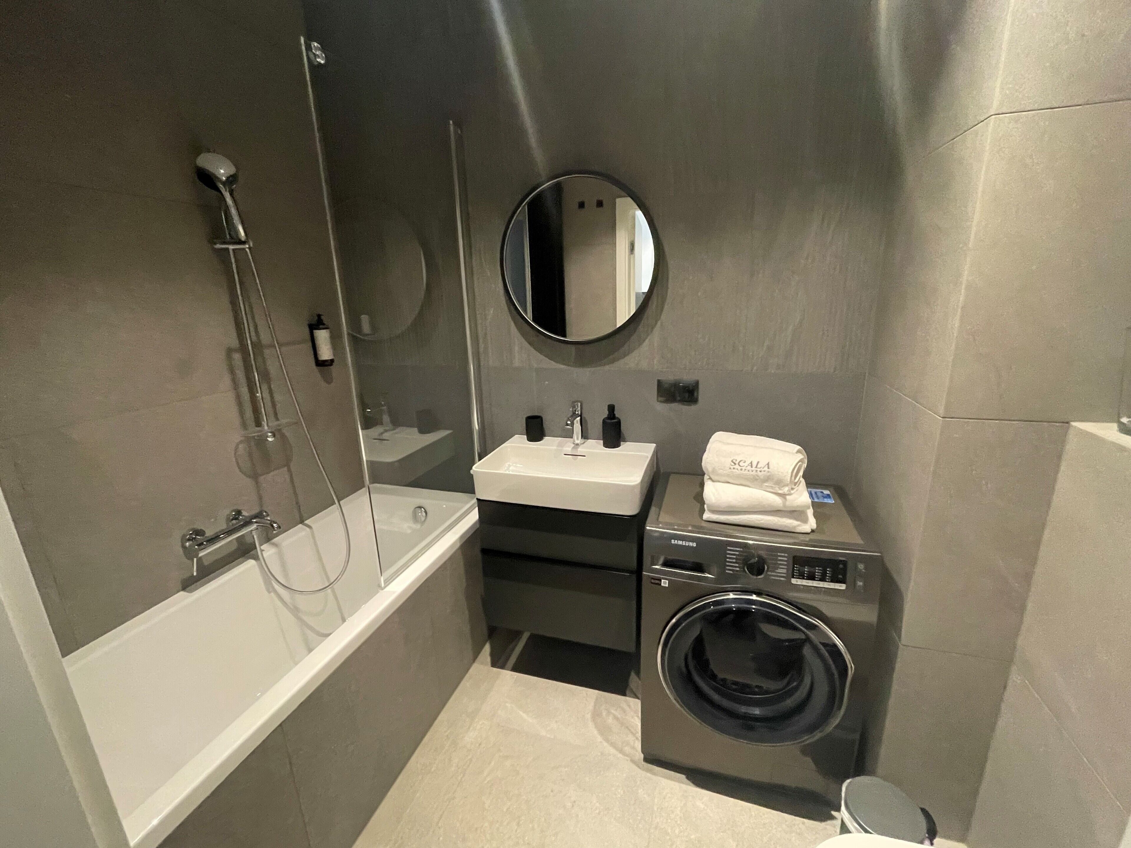 Un baño pequeño con bañera, lavabo, espejo y lavadora.