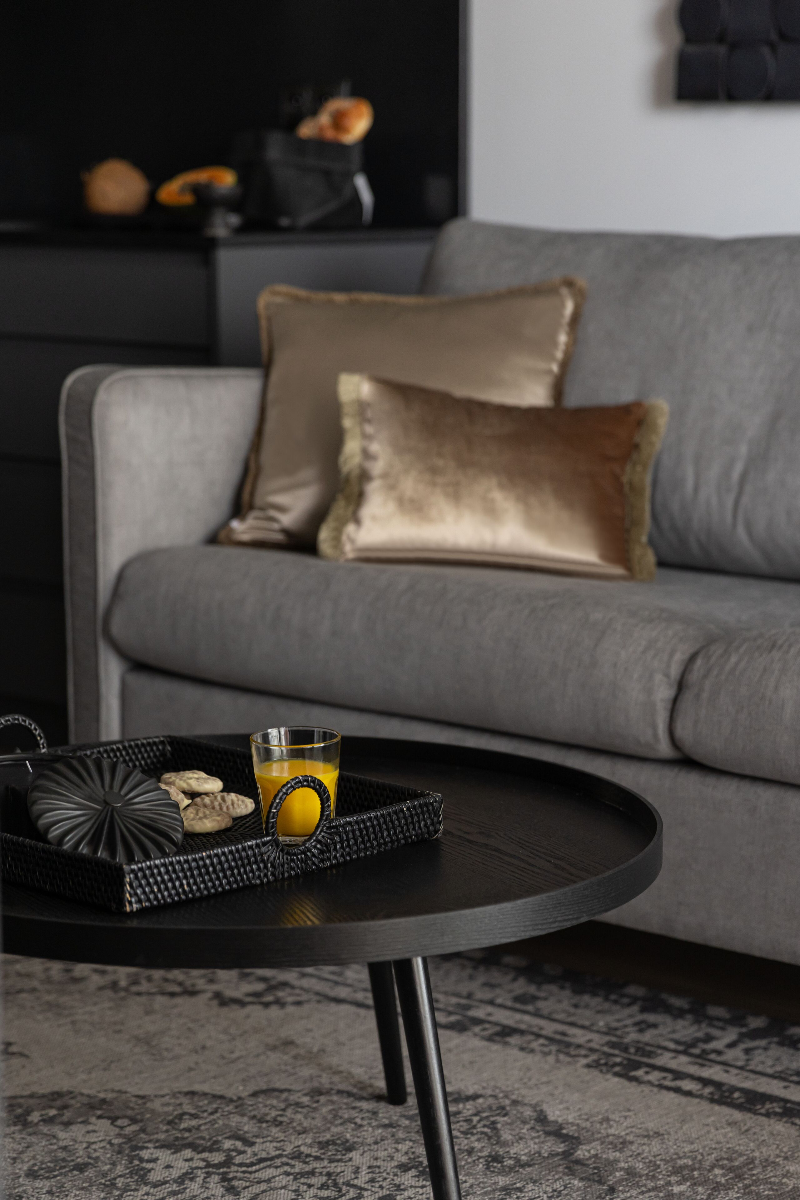 Ein modernes Wohnzimmer mit einem grauen Sofa, einem schwarzen Couchtisch und einer Platte mit Keksen und einem Glas Orangensaft.