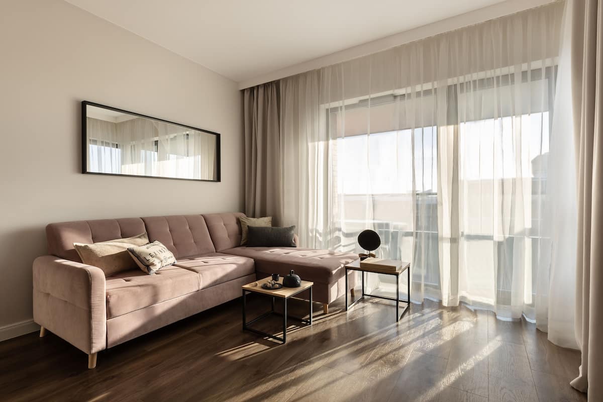 A modern living room with a sectional sofa, a coffee table, and a large window with sheer curtains.