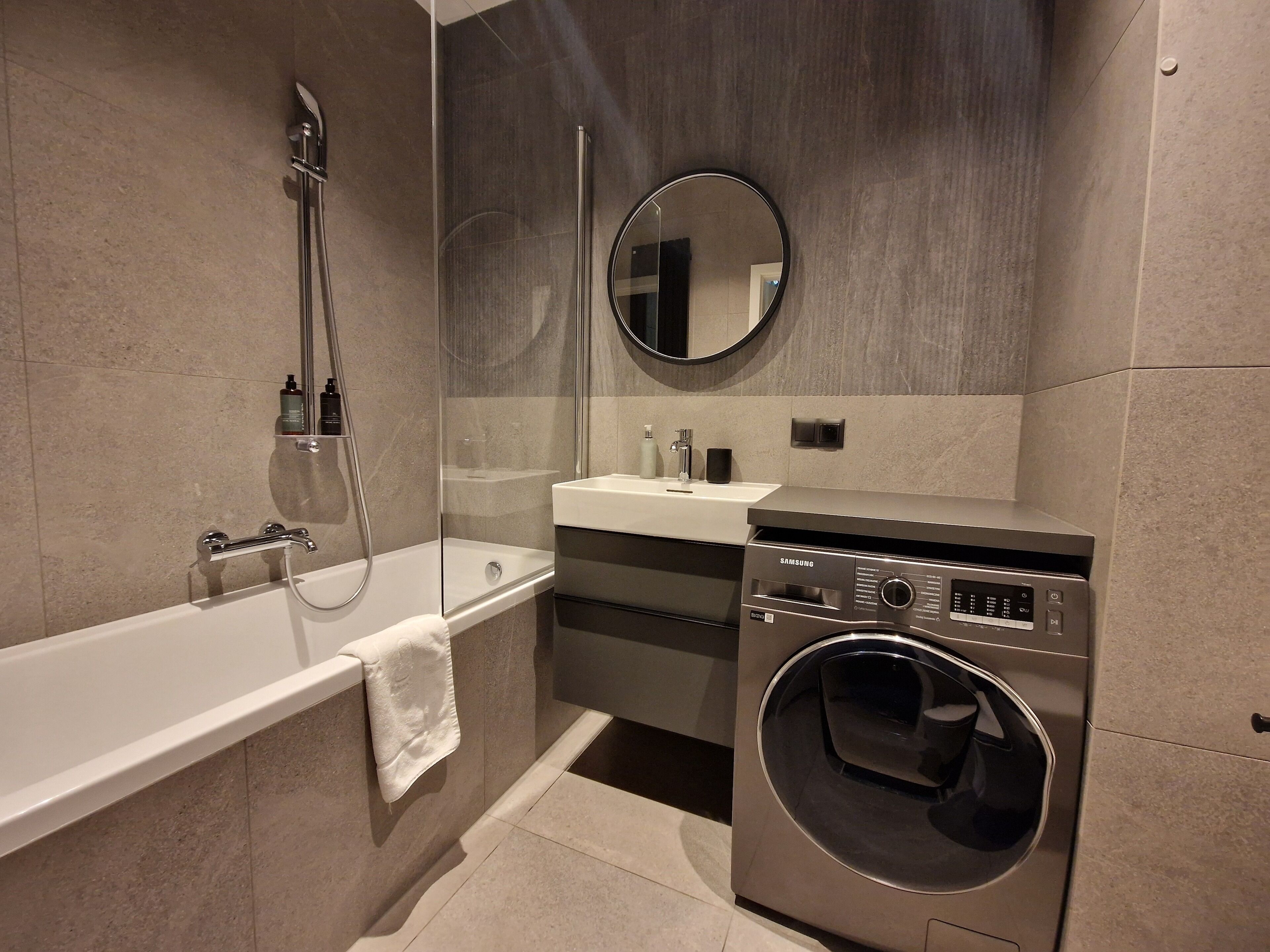 Un baño moderno con bañera, ducha con mampara de vidrio, lavamanos y lavadora y secadora integradas.