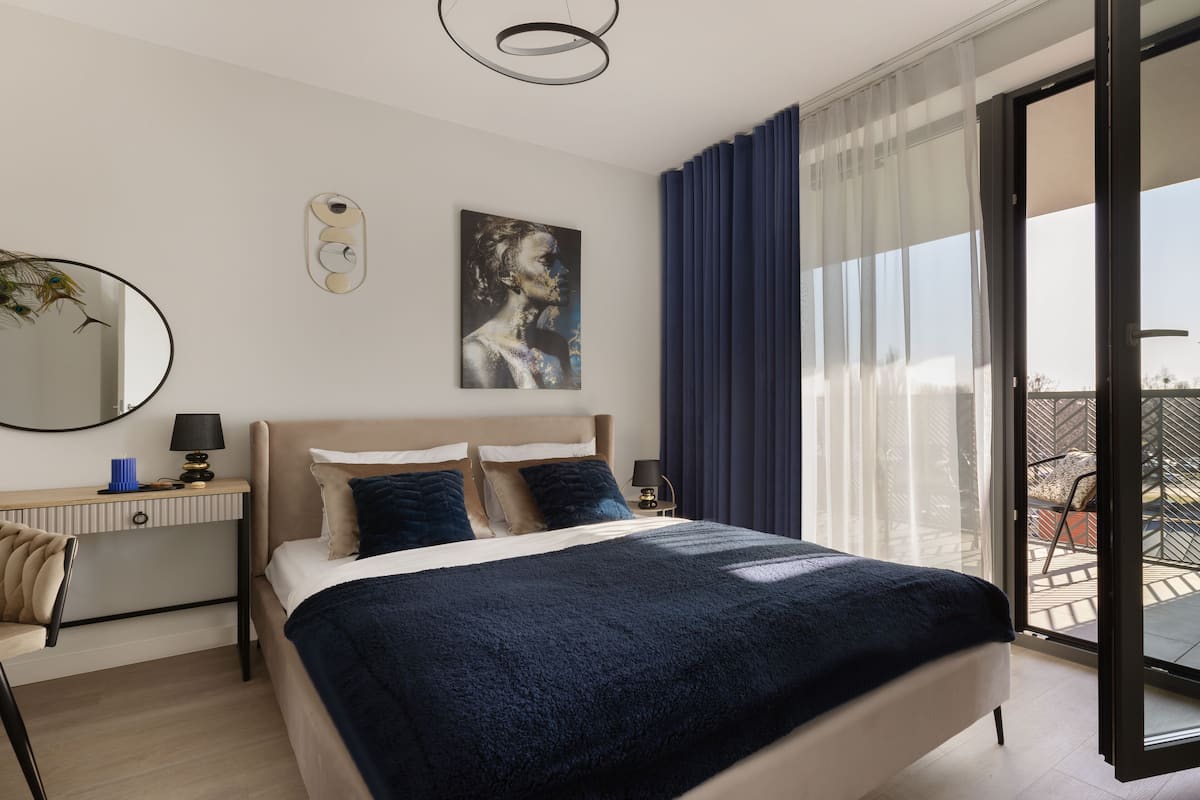 A modern bedroom with a large bed, a desk, and a view of the outdoors.
