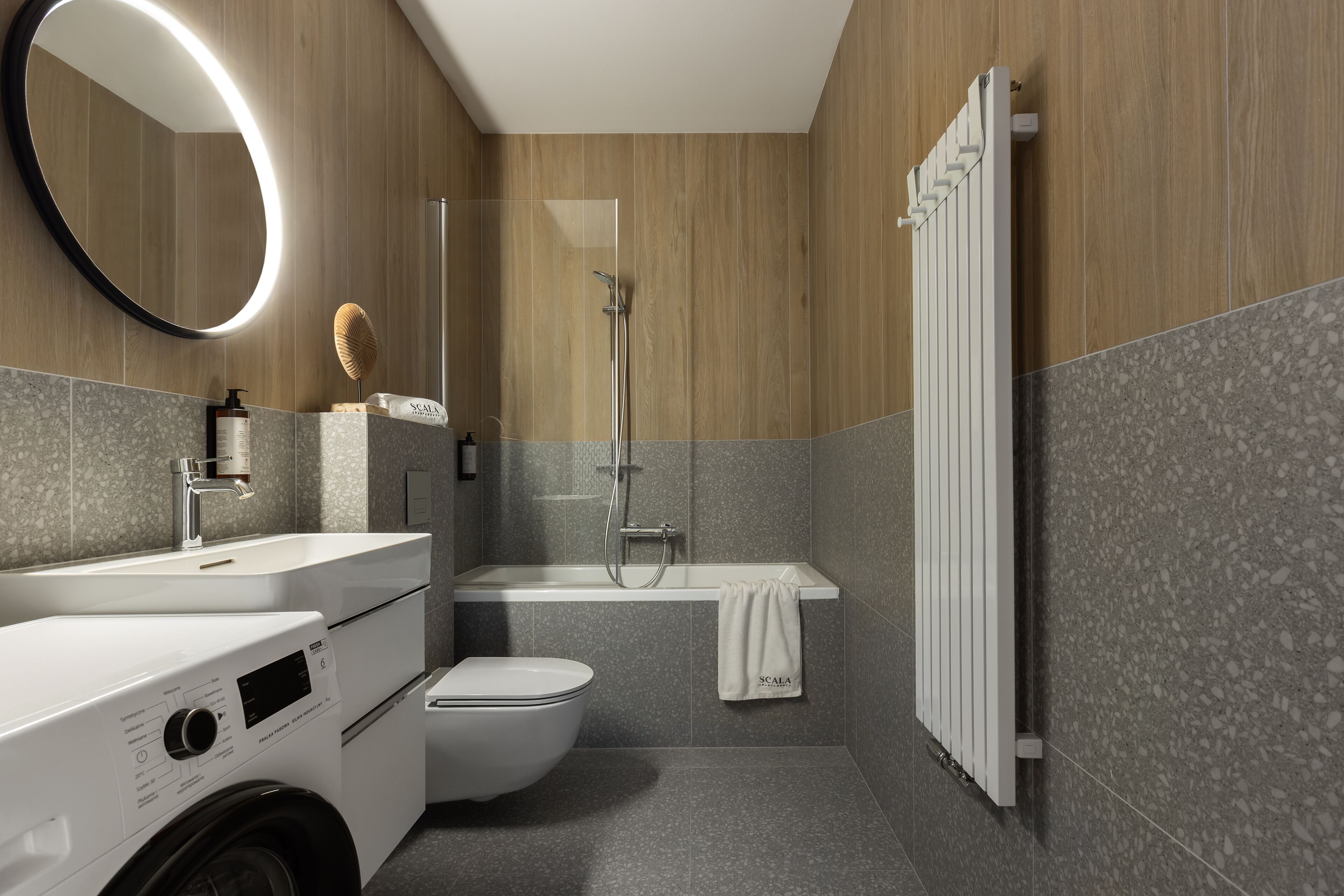 Une salle de bain moderne équipée d’un lave-linge, de toilettes, d’une baignoire et d’une douche à parois de verre.