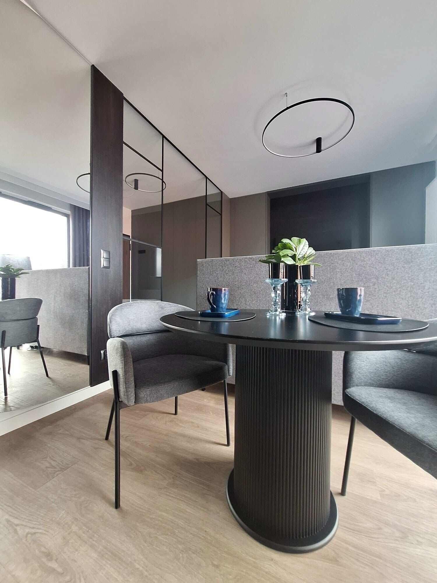 A modern dining area with a round table, grey upholstered chairs, and a potted plant.