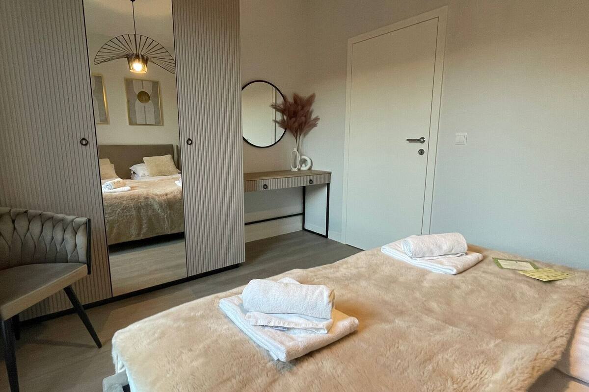 A modern hotel room with a large bed, a sitting area, a mirror, and a small desk.