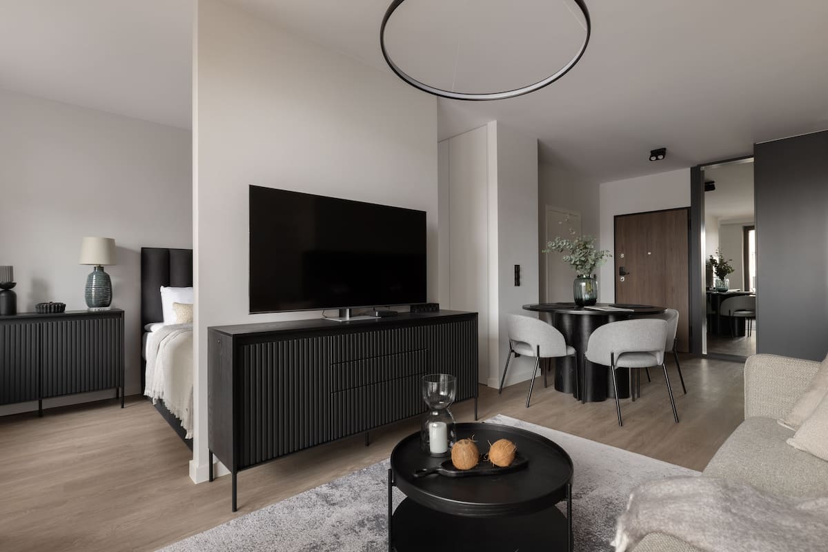 A modern living room with a large flat-screen TV, a dining area with two chairs, a coffee table with two coconuts, and a sofa.