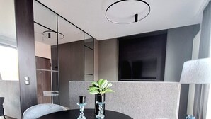 Un espace repas moderne avec une table ronde noire, deux chaises grises à revêtement rembourré, une plante en pot et un grand lampadaire.