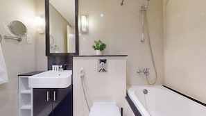 A modern bathroom with a white sink, a mirror, a shower, and a small potted plant.
