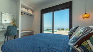Un dormitorio con una cama grande, un escritorio, una silla y vista al mar a través de una puerta corrediza.