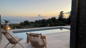 Zona de piscina con dos sillas de mimbre y vistas al mar al atardecer.