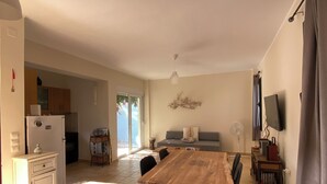 Een ruime eethoek met een houten tafel en stoelen, een keuken op de achtergrond en een televisie aan de wand.