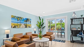 A room with four brown leather sofas, a round coffee table, and a large potted plant. There is a painting of a beach scene on the wall, and a bookshelf with various items. - Peaceful Tropical Escape with Heated Pool Near Fort Lauderdale Beach! (Fort Lauderdale)