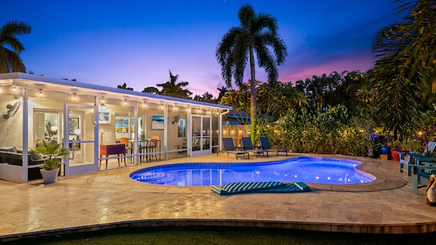 A swimming pool area with a covered patio, lounge chairs, and a palm tree. - Peaceful Tropical Escape with Heated Pool Near Fort Lauderdale Beach! (Fort Lauderdale)