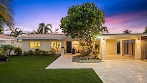 A modern house with a well-maintained lawn, a paved driveway, and a large tree in the front yard. - Peaceful Tropical Escape with Heated Pool Near Fort Lauderdale Beach! (Fort Lauderdale)