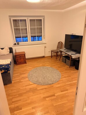 Una habitación con cama, escritorio con computadora, silla, radiador y ventana con persianas.