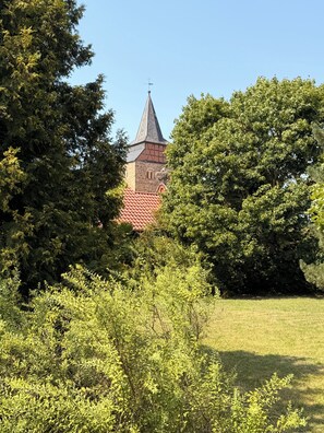 Una iglesia con un campanario puntiagudo, rodeada de vegetación exuberante y un cielo despejado.