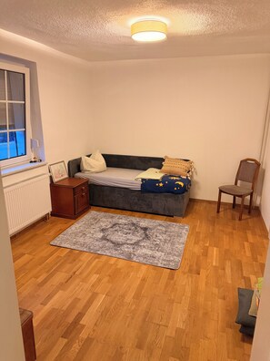 Un dormitorio con una cama, una silla, un radiador y una ventana.