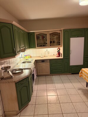 Cuina amb armaris verdosos, un rentaplat, una cafetera i un frigorífic.