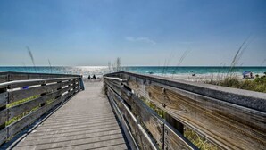 Una passerella in legno conduce a una spiaggia con cielo sereno e acque calme.