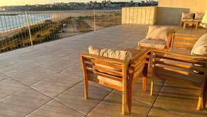 Eine Dachterrasse mit Holzmöbeln und Blick auf Stadt und Strand.