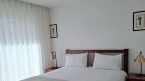Ein ordentlich bezogenes Bett mit weißen Leinen in einem Zimmer mit Holzboden.