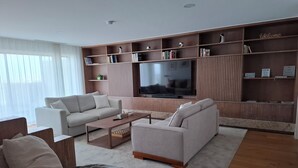 Ein modernes Wohnzimmer mit einem großen Flachbildfernseher, zwei Sofas, einem Couchtisch und einem Bücherregal mit einem 'Welcome'-Schild.