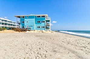Un hôtel situé en bord de mer, avec plusieurs étages, un balcon et une plage de sable en premier plan.