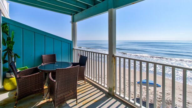 A covered outdoor seating area with wicker furniture and a view of the ocean.