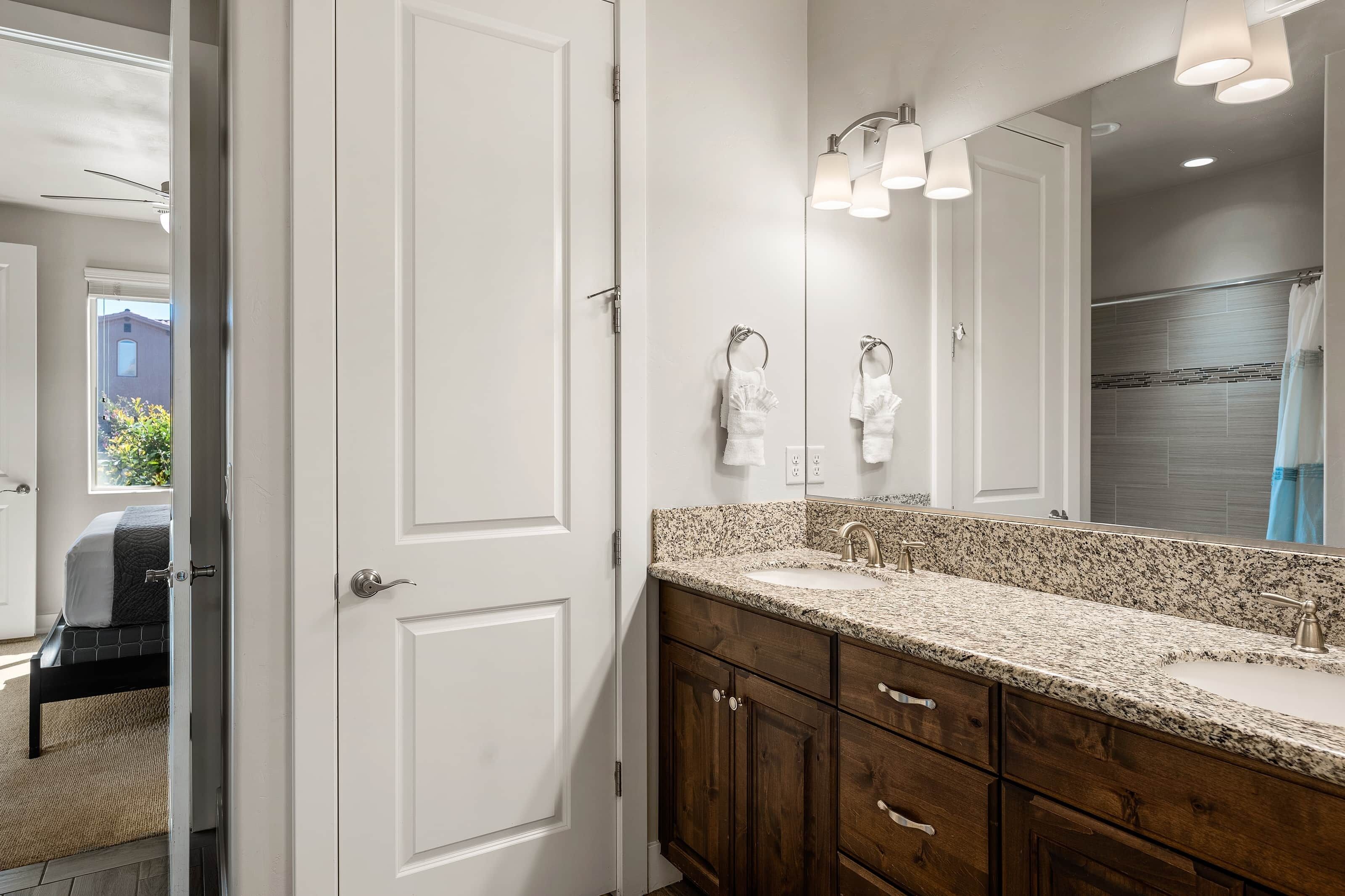 A bathroom with a granite countertop, a large mirror, and a shower area.