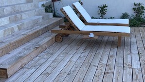 En træterrasse med en loungeseng i træ og et lille bord med kop og underkop.