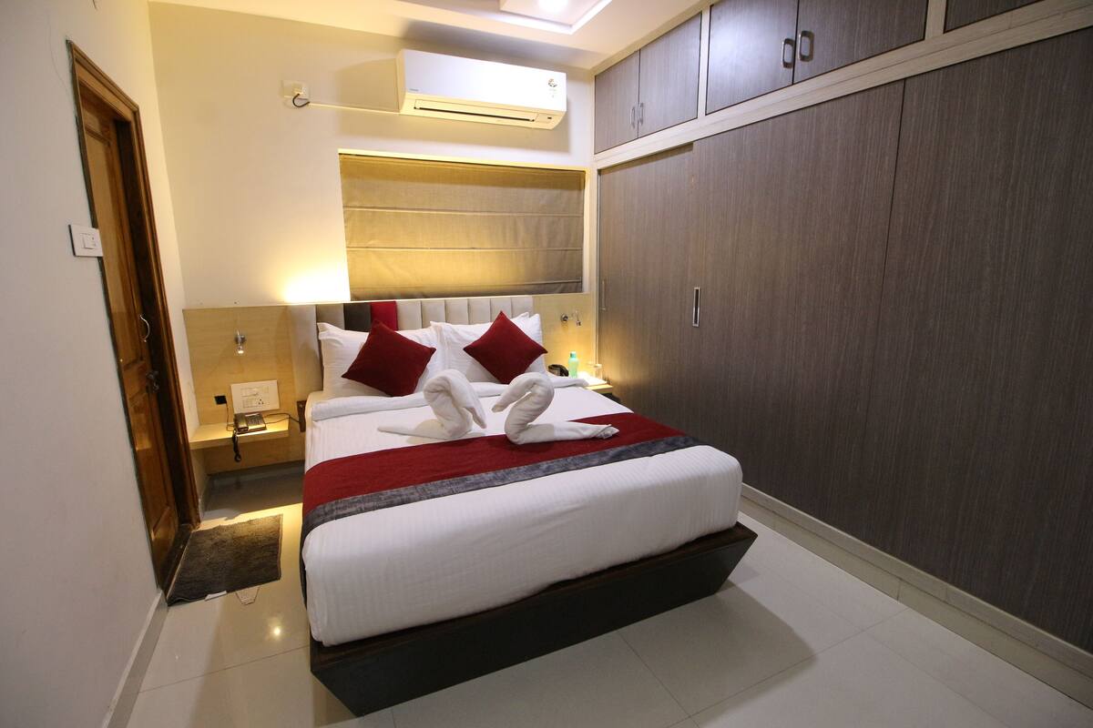 Een hotelkamer met een groot bed, een kledingkast, een airconditioning en een nachtkastje met een lamp.