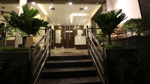 Eine Treppe führt zu einem Empfangsbereich mit Glastüren, Topfpflanzen und einem modernen Interieur.