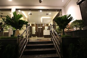 Eine Treppe führt zu einem Empfangsbereich mit Glastüren, Topfpflanzen und einem modernen Interieur.